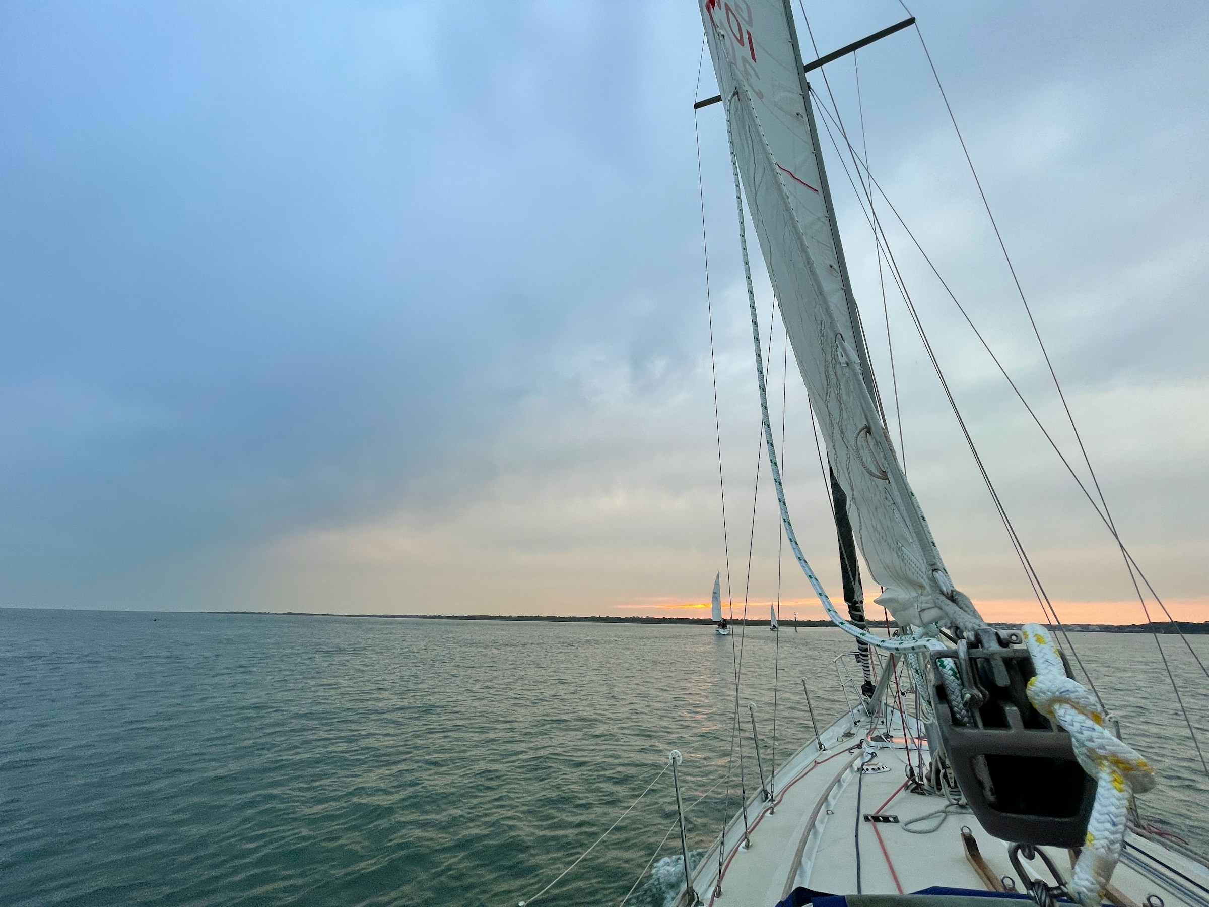 Proa de un barco de vela sobre aguas abiertas y la costa al fonde.