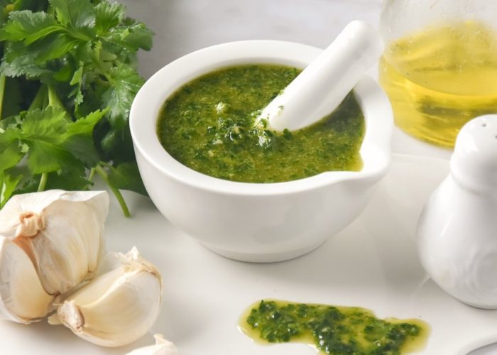 Ingredientes para hacer el mojo verde canario y un mortero blanco con la salsa preparada.