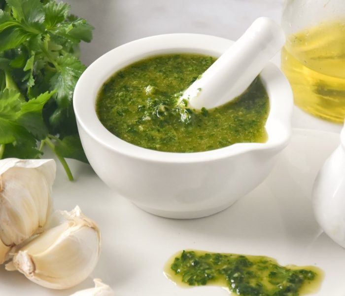 Ingredientes para hacer el mojo verde canario y un mortero blanco con la salsa preparada.