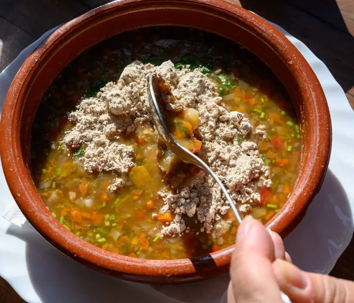 Potaje en cuenco de barro con gofio espolvoreado por encima.